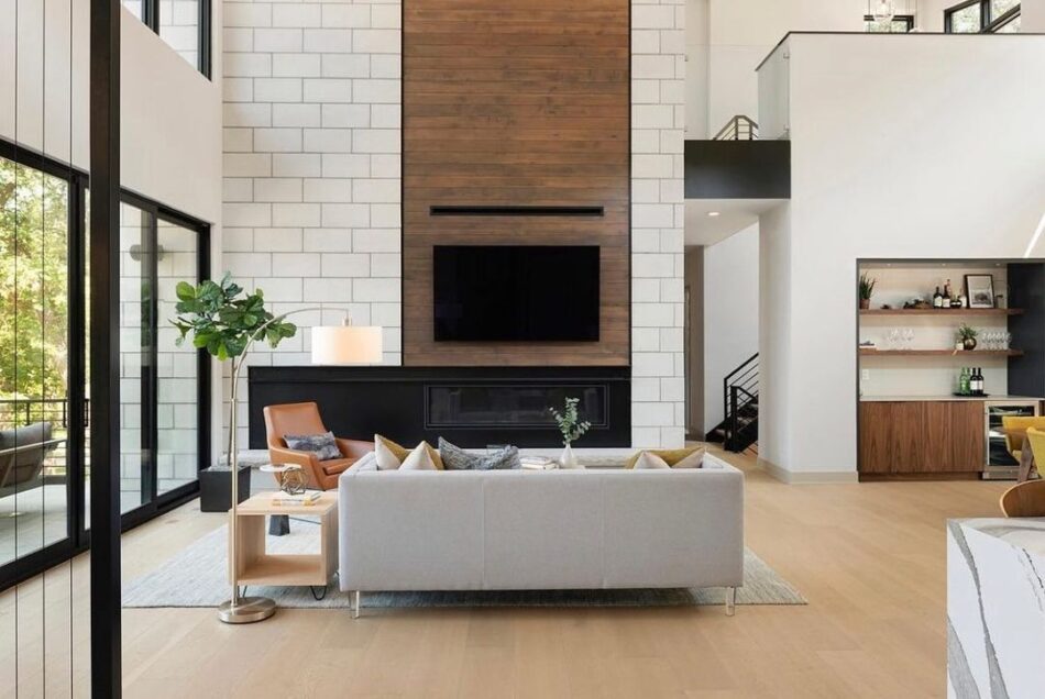 This living room area features a gray sofa, a leather chair and light hardwood floors. A television is mounted to the wall.