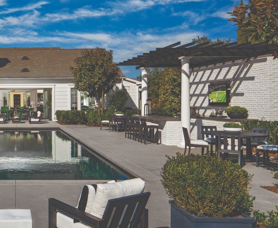 Backyard with brick veneer outdoor kitchen and bar, topped with pergola sitting on two columns.