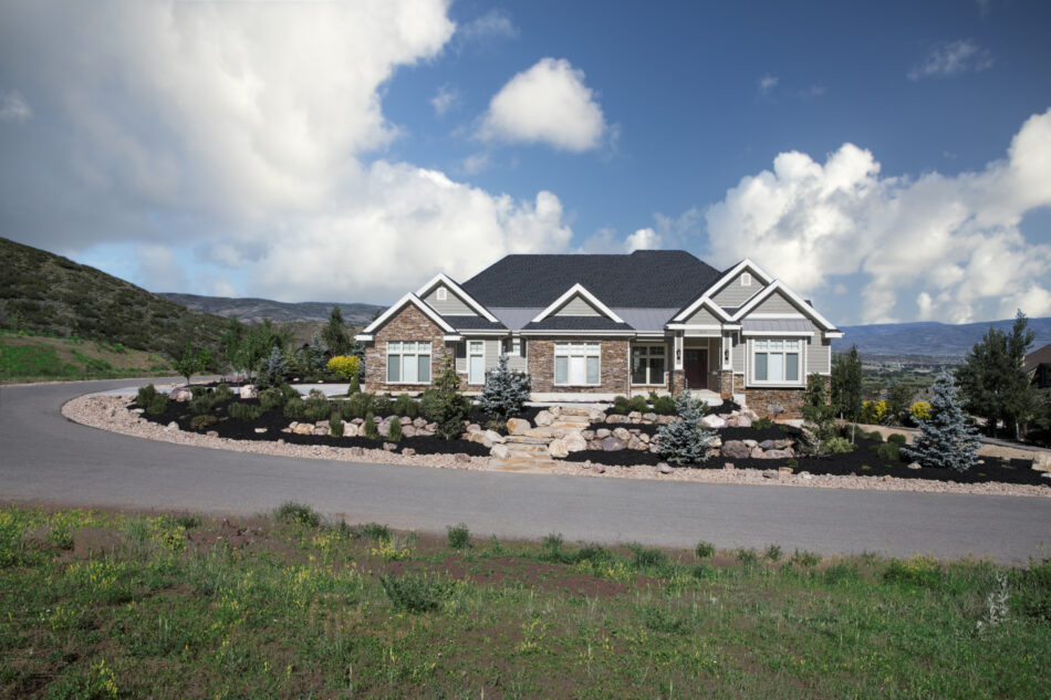 A home at a high elevation with a backdrop of the mountainscape. The home has a front yard with a combination of stones and pine trees.