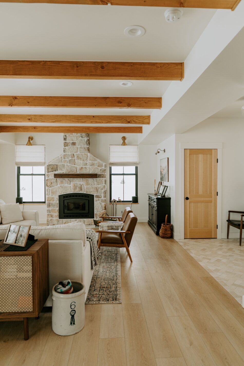 A neutral living room with light hardwood flooring, an exposed stone fireplace and exposed beams.