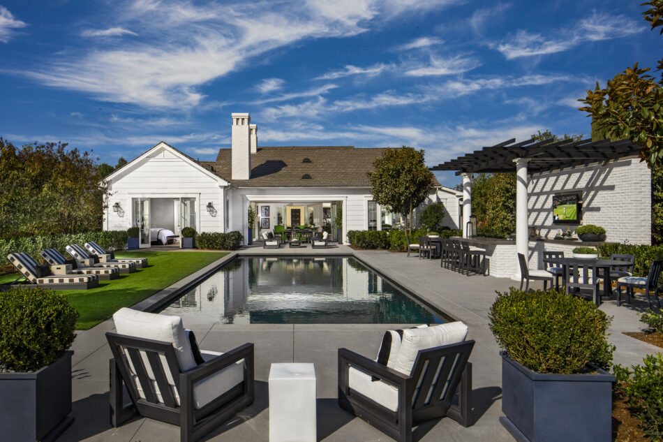 Backyard entertainment space with outdoor kitchen utilizing white brick veneer siding and white columns supporting dark wooden pergola beams.