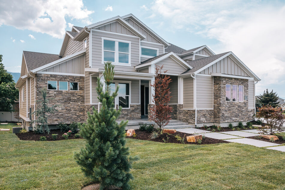 The view of the front of a home. The home has exposed stone and white trim with a large front yard and front walkway.