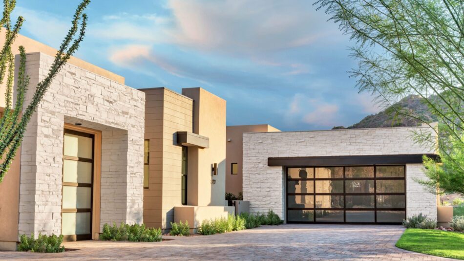 A modern home with accents of white stacked stone veneer siding. The home also incorporates large panel windows and doors.