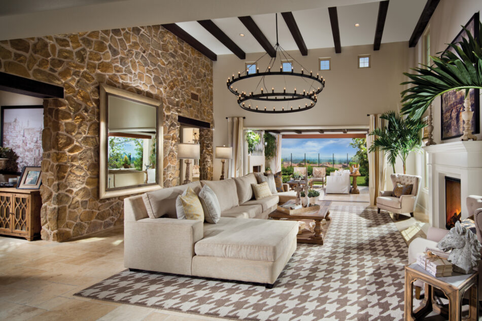 Large living room with stone veneer accent wall, sectional couch, large chandelier and an open wall looking out to a city beyond.