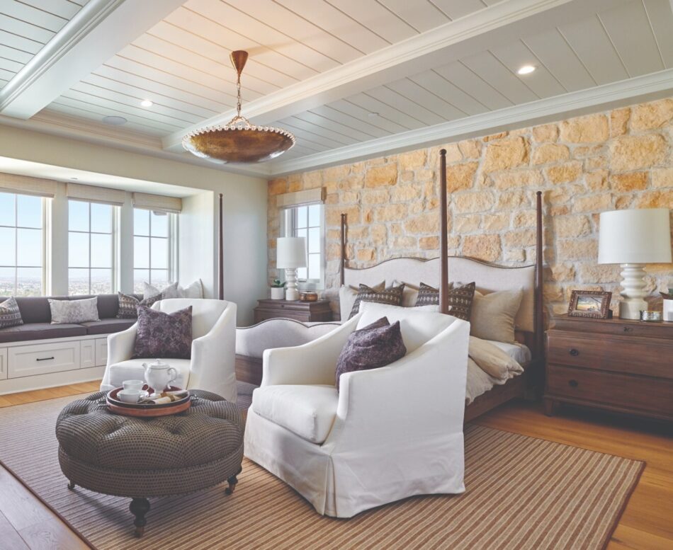 Large master bedroom with accent wall of stone veneer behind a four post bed.