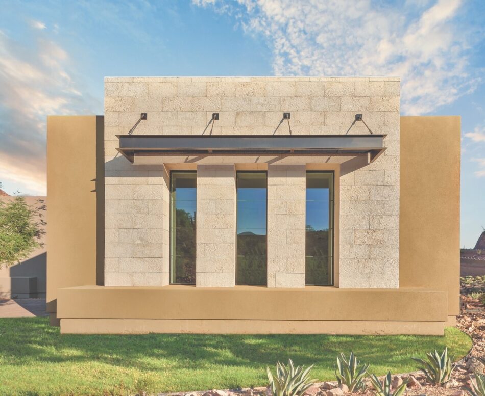 The desert home features strong linear lines accented by cut rectangular stone, vertical windows and sand colored smooth plaster.