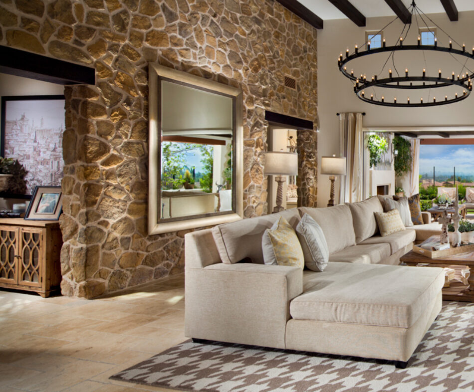 Large living room with masonry veneer accent wall, sectional couch, large chandelier and an open wall looking out to a city beyond.