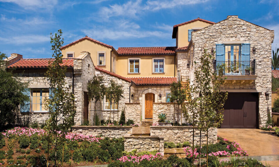 Spanish-style home with red barrel roof tiles, stucco, and white stone veneer sits behind a garden of pink flowers.