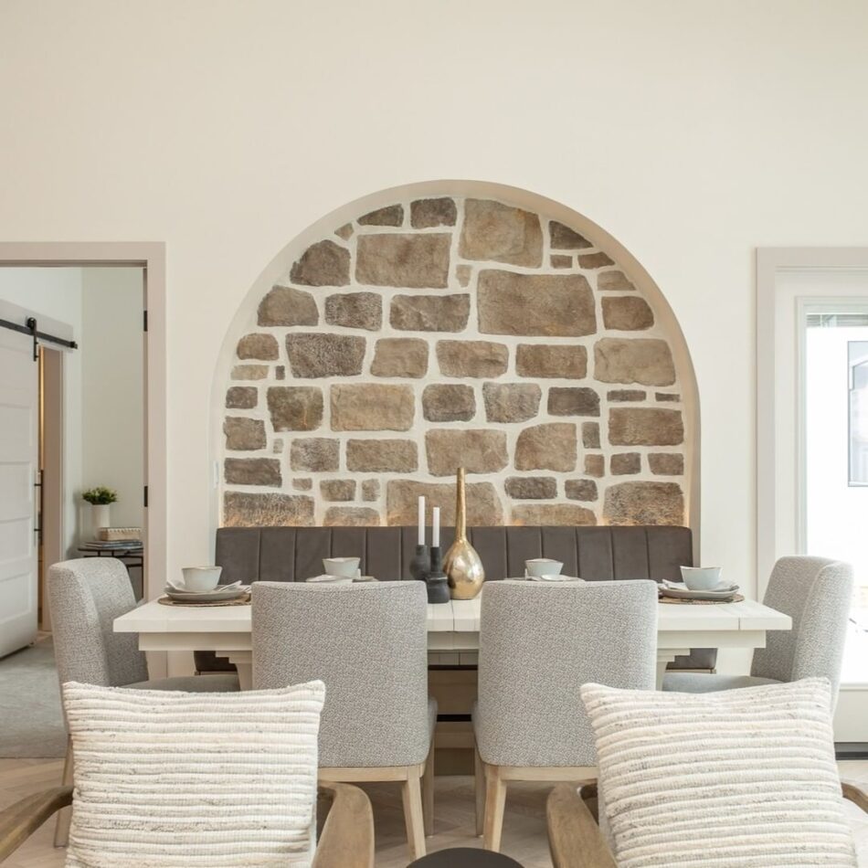 A dining room featuring an interior stone veneer accent wall with a dining room table, a bench and four gray chairs.