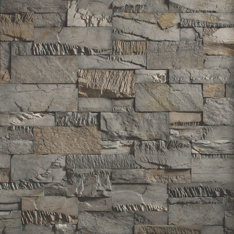 An image of a dark gray and tan stone wall. The wall is made of chopped stone and the pieces of stone are a variety of sizes.